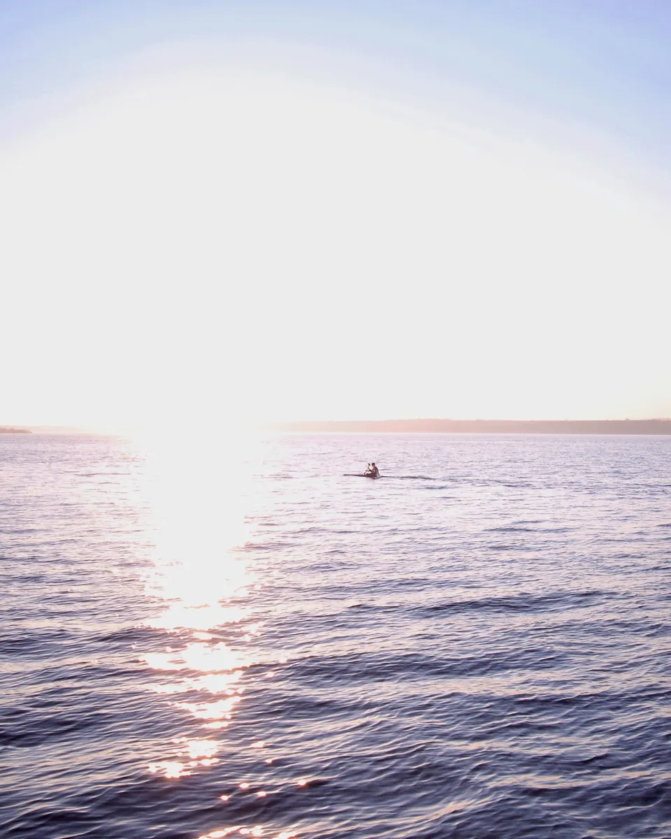 Kayaker moving across calm water at sunrise